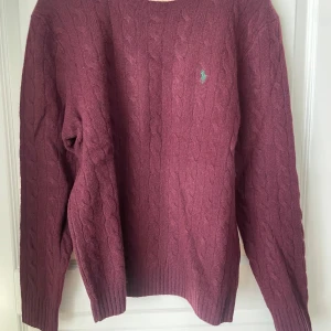 Vinröd stickad tröja från Polo Ralph Lauren - Säljer en snygg vinröd stickad tröja från Polo Ralph Lauren. Tröjan har ett klassiskt flätmönster och en liten broderad logga på bröstet. Perfekt för kyliga dagar! Nypris - 2 695