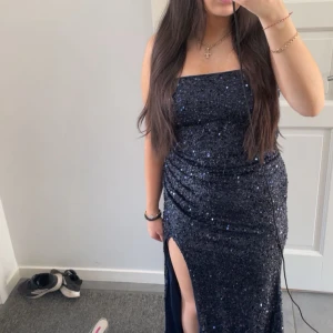 Mörkblå glittrig långklänning - Säljer en snygg mörkblå långklänning med glittriga paljetter. Klänningen är ärmlös, har rak urringning och en hög slits på ena sidan. Perfekt för bal eller fest och ger en riktigt glam känsla.
