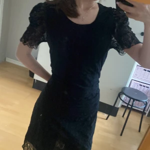 Svart spetsklänning från Sisters Point - Supersnygg svart kortklänning från Sisters Point med puffiga spetsärmar och rund halsringning. Klänningen har fina spetsdetaljer över hela tyget och är figurnära i modellen. Perfekt för dig som vill sticka ut med en elegant och trendig look. Passar S-M