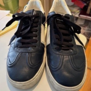 Valentino flycrew - Snygga sneakers från Valentino flycrew i svart och vitt skinn med coola nitar baktill på sulan. Klassisk låg modell med svarta snören och vit panel på sidan. Perfekta för dig som vill sticka ut med exklusiva detaljer och streetkänsla.