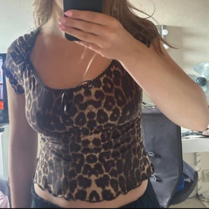 Leopardmönstrad topp - Säljer en croppad topp med leopardmönster och korta ärmar. Toppen har en söt liten svart rosett vid den rundade urringningen.❤️Den är i storlek L men passar även M.