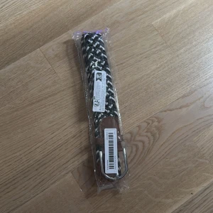 Svart och vit flätad bälte - Snyggt flätat bälte i svart och vitt med bruna skinn-detaljer vid spännet. Bältet har ett klassiskt silverfärgat spänne och passar perfekt till jeans eller chinos. Kommer i originalförpackning och har en modern, stilren look.