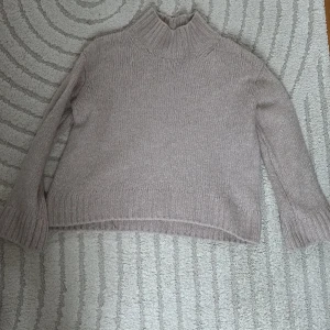 Beige/gammelrosa stickad polotröja - Mysig beige stickad polotröja med ribbade muddar och hög krage. Tröjan har en rak och något boxig passform med långa ärmar. Perfekt för lager-på-lager och chill höst- och vinterstil.