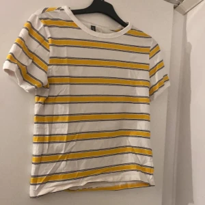 Randig t-shirt från H&M Divided - Vit t-shirt med gula och svarta horisontella ränder från H&M Divided. Klassisk rund halsringning och korta ärmar. Skön och lätt i bomull, perfekt för en chill look. Passar dig som gillar färg och enkel stil.