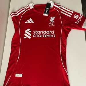 Liverpool FC Hemma tröja 25/26 - You'll never walk alone – och du gör det definitivt inte i fel tröja! Hos BallerDrip hittar du Liverpool-tröjor i alla storlekar, för både stora och små fans. Perfekt för matchdagar, träning eller bara för att bära klubbens färger med stolthet.  ✅ Alla storlekar finns – från barn till vuxen ✅ Bästa kvaliteten i hela Sverige ✅ Snabba leveranser & schyssta priser  Det finns ingen bättre kvalitet i Sverige – vi snackar äkta drip för riktiga supportrar. Passa på innan de säljer slut!