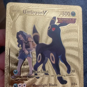 Umbreon V (Pokémonkort) - Coolt och glittrande Pokémonkort med Umbreon V och en tränare. Perfekt för samlare och fans av Pokémon! Korten har en exklusiv guldfinish och är ett måste för dig som vill sticka ut i samlingen.