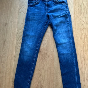 Slim blå jeans i storlek 30/34 - Snygga slim fit jeans i klassisk blå tvätt med lätt slitning. Modellen har smal passform och fem fickor, perfekta för en clean och modern look. Jeansen är tillverkade i stretchigt denimtyg som sitter skönt hela dagen.