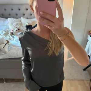 Mörkgrå offshoulder topp Gina Tricot - Snygg mörkgrå offshoulder topp från Gina Tricot i mjukt och lätt material. Långärmad modell med avslappnad passform, perfekt för dig som gillar en stilren och trendig look. Passar till både jeans och kjol för en cool vibe.