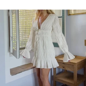 Vit kortklänning med volangärm - Superfin vit kortklänning med v-ringning, långa volangärmar och knyt i midjan. I nyskick men utan prislapp, aldrig använd! Slutsåld på hemsidan🥰nypris:699