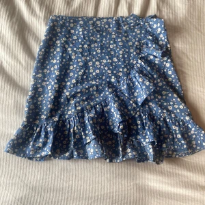Två korta kjolar med volang och mönster - Säljer två superfina kortkjolar med volangkant och omlottkänsla. Ena är blå med små vita blommor, den andra är vit med svarta prickar. Båda har en söt rosettdetalj upptill och är perfekta för sommarens alla tillfällen. 75 kr st, 120 för båda men pris kan även diskuteras 💕💕