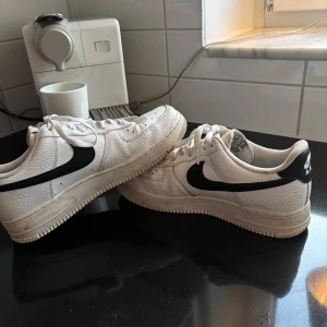 Nike Air Force 1 vita sneakers med svart swoosh - Klassiska Nike Air Force 1 sneakers i vitt skinn med svart swoosh. Säljer ut lite grejer från garderoben som bara står. Dessa är nog använda runt 20/25 gånger om jag får gissa. Lite smutsiga men annars i toppskick