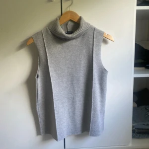 Grå stickad väst från Zara - Säljer en grå stickad väst från Zara med hög, ribbad polokrage. Västen är ärmlös och har en rak, loose passform som ger en chill vibe. Perfekt att slänga över en skjorta eller långärmad tröja för en snygg lager-på-lager-look.