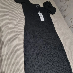 Svart smockad klänning Gina Tricot M - Supersnygg svart smockad klänning från Gina Tricot i storlek M. Klänningen har puffiga korta ärmar och en tight smockad passform som ger en cool och trendig look. Perfekt för dig som gillar stilrena och enkla plagg med det lilla extra.