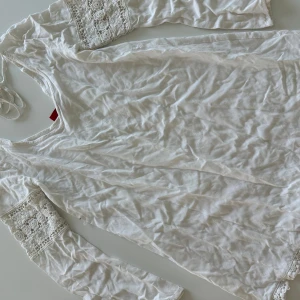 Vit blus med spetsdetaljer - Superfin vit blus med långa ärmar och vackra spetsdetaljer på ärmarna och längs kanten. Blusen har en romantisk vibe med broderade blommor i spetsen och är gjord i mjuk bomull. Perfekt för dig som gillar en feminin och bohemisk stil.