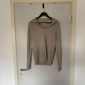 Beige stickad half zip från Jack & Jones - Ribbstickad beige tröja från Jack & Jones med halv dragkedja och krage. Perfekt för lager-på-lager och chill stil. Långärmad och i mjukt material som håller dig varm under kyliga dagar.