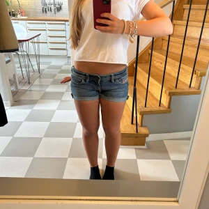 Blå jeansshorts  - Snygga blå jeansshorts från Diesel med låg midja. Shortsen är perfekta för sommaren. Jag har på de fyra första bilderna vikt upp bensluten, men man kan på bild fem se den egentliga längden. Midjemåttet är 38 cm,  längden är 26 cm och grenen är ca 17 cm. Deras originella storlek är W 27 L 30. 