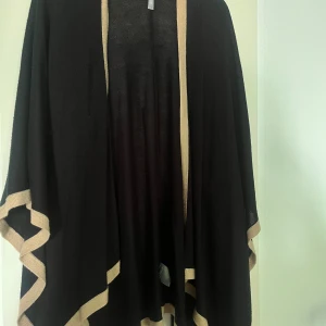 Svart poncho med beiga detaljer  - Säljer denna svarta ponchon med beiga detaljer från Åhléns. Den är använd men i väldigt bra skick. Den är i one size. Relativt tunt material. 