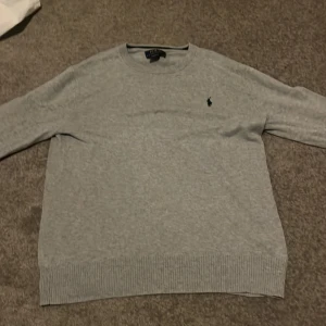 Grå bomullströja från Polo Ralph Lauren - Snygg grå tröja från Polo Ralph Lauren i mjuk pima bomull. Klassisk rund halsringning, ribbade muddar och diskret broderad logga på bröstet. Perfekt basic som funkar till allt och är superbekväm med lång ärm och normal passform.