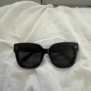 Svarta solglasögon från Ray-Ban - Snygga svarta solglasögon från Ray-Ban med klassisk fyrkantig form och guldiga detaljer vid skalmarna. Perfekta för att lyfta vilken outfit som helst och ger en cool vibe. Ikonisk logga på sidan och bekväm passform.