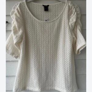 Vit stickad blus med volangärmar - Superfin vit stickad blus från lindex med korta volangärmar och rund halsringning. Mjuk struktur och diskret mönster i tyget ger en söt och trendig look. Perfekt att matcha med jeans eller kjol för en fräsch stil.