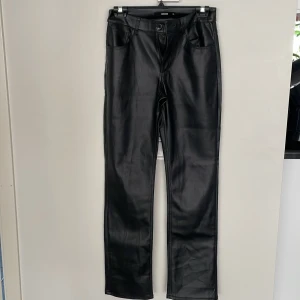 Svarta skinnbyxor från BikBok - Snygga svarta byxor i skinnimitation från BikBok. Klassisk femficksmodell med raka ben och normal midja. Byxorna har bälteshällor och stängs med knapp och dragkedja. Perfekta för en edgy look.
