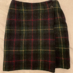 Rutig ullkjol från Talbots - Mörkgrön och svart rutig kjol från Talbots i 100% ull med inslag av röda och gula rutor. Klassisk rak modell med knäppning i sidan och helfodrad insida i polyester. Perfekt för dig som gillar preppy och tidlös stil.