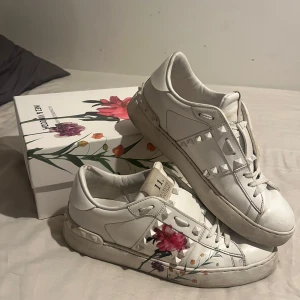 Valentino Rockstud sneakers med blommor - Snygga vita Valentino Rockstud sneakers collab med Inez & Vindoodh. Ikoniska nitar och blommigt mönster på sidorna. Storlek 38.  Perfekta för dig som vill sticka ut med en lyxig och kreativ vibe. Nypris 7075kr. Pris kan diskuteras vid snabb affär💗