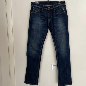 Mörkblå Replay jeans straight fit - Snygga mörkblå jeans från Replay i klassisk straight fit. Jeansen har slitna detaljer, kontrastsömmar och fem fickor. Märkeslogga på fickan och bak på linningen. Perfekta för dig som gillar en tidlös och avslappnad look.