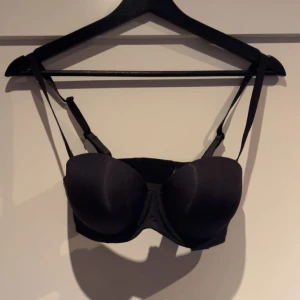 Svart korsett-topp från Boohoo - Svart korsett-topp från Boohoo med vadderade kupor och justerbara axelband. Snygg och enkel design som ger en clean siluett. Perfekt att styla under en skjorta eller som den är till jeans eller kjol. Helt oanvänd, storlek 34 B