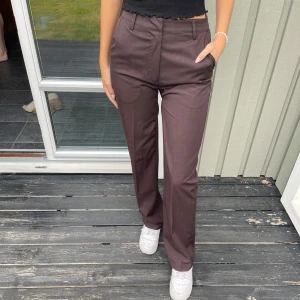 Bruna kostymbyxor - Snygga bruna kostymbyxor med raka ben. Materialet känns mjukt och har en lätt glansig finish. Byxorna är långa och passar mig som är 171cm