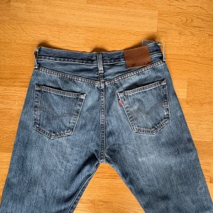 Levi's 501 blå jeans 30/30 - Klassiska blå Levi's 501 jeans med raka ben och normal passform. Jeansen har fem fickor, knappgylf och den ikoniska läderpatchen bak i midjan. Tillverkade i slitstarkt bomullsjeans med snygg tvättad finish och röda Levi's-tag på bakfickan. Inga defekter