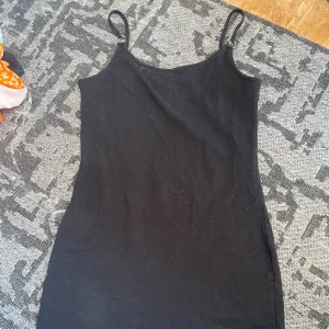 Svart kort klänning från Sinsay - Enkel svart kort klänning från Sinsay med smala axelband och rak passform. Perfekt basplagg som är lätt att styla med accessoarer. Tillverkad i mjukt material som känns skönt mot huden.