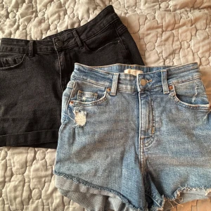 Två par jeansshorts, blå & svarta - Säljer två par snygga jeansshorts! Ett par ljusblå med slitningar och fransig kant, klassisk femficksmodell. Det andra paret är svarta, också i jeans, med uppvikta benslut och enkel design. Perfekta för sommaren och chill dagar.