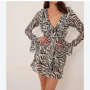 Klänning Zebramönster - Supersnygg kort omlottklänning från NA-KD med zebramönster i svart och vitt. Klänningen har volangdetaljer, v-ringning och långa ärmar🌸 Perfekt sommarklänning🌸 I nyskick🌸 Slutsåld online