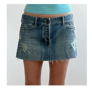 Jeanskjol med slitningar och paljetter - Cool kort jeanskjol med rå kant, slitningar och paljett-detaljer. Klassisk blå denim med bälteshällor och knappstängning framtill. Perfekt för dig som gillar en edgy och trendig stil.