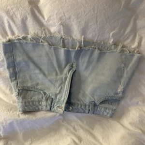 Ljusblå mini kjol med fransad kant - Ljusblå mini denim kjol  med fransad, rå kant upptill och detaljer som fickor och knapp framtill. Perfekt för dig som vill sticka ut med en edgy och kreativ stil.