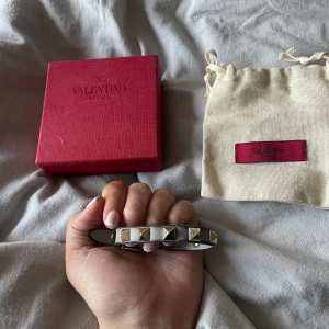 Valentino Garavani Rockstud armband - Snyggt armband från Valentino Garavani i grått skinn med ikoniska pyramidformade nitar i silverfärg. Justerbart spänne och stilren design! Kommer med originalröd förvaringspåse från Valentino. Pris kan diskuteras 💗