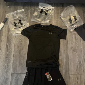 Svart tränings-tshirt från Under Armour - Svart kortärmad tränings-tshirt från Under Armour med diskret mönster och logga på bröstet. Tillverkad i lätt och ventilerande syntetmaterial som passar perfekt för löpning eller gym. Snygg sportig look med modern passform.