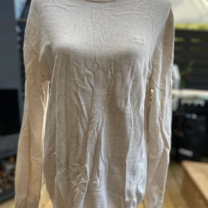Beige stickad tröja från Esprit M - Beige tröja med rund halsringning och långa ärmar. Tröjan har en liten Esprit-logga på bröstet. Halsringningen har en dekorativ detalj med ränder i olika färger. Längd: 74 cm ﻿Bystvidd: 56 cm ﻿100% bomull.  Inga bilder när den sitter på mig! Katter finns i hemmet!