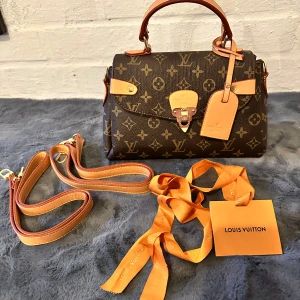 Louis Vuitton Monogram axelväska - Säljer en klassisk Louis Vuitton axelväska i brunt monogrammönster med beige och bruna skinn-detaljer. Väskan har både handtag och avtagbar axelrem, samt flera fack inuti. Ikonisk LV-logga och snygga metalldetaljer framtill. Perfekt för dig som gillar lyxig och tidlös design.