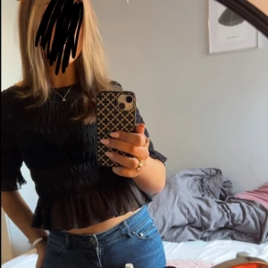 Svart blus med volang från Gina Tricot - Supersöt svart blus från Gina Tricot med smockad struktur över hela toppen och volangkant nertill. Halvlånga ärmar och rund halsringning. Köpt här från plick! 💕