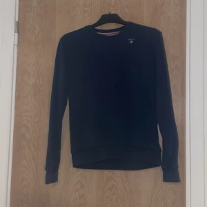 Mörkblå sweatshirt från GANT - Snygg mörkblå sweatshirt från GANT med broderad logga på bröstet. Tröjan har rund halsringning, långa ärmar och ribbade muddar. Tillverkad i mjuk bomull som är skön att ha på sig. Perfekt för en chill och stilren look. Storlek är 158-164 är till 13-14 åringar skriv om ni är intresserade och om ni vill ha mindre pris. Tack