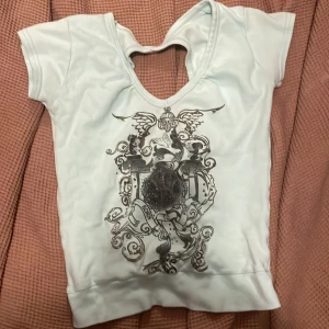 Vit omlottopp med tryck och cut out - Snygg vit topp med korta ärmar, coolt svart tryck framtill och unik omlottdesign i ryggen med cut out-detalj. Materialet känns mjukt och stretchigt, perfekt för dig som gillar att sticka ut. Passformen är normal.