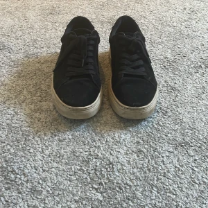 Svarta sneakers med mockadetaljer - Snygga svarta vagabond sneakers med ovandel i mocka och klassisk snörning. Skorna har en vit, något chunky sula som ger en cool kontrast mot det svarta. Perfekta för dig som gillar en stilren och urban look. Storlek 39 men lite stor i storleken. Kan diskutera pris