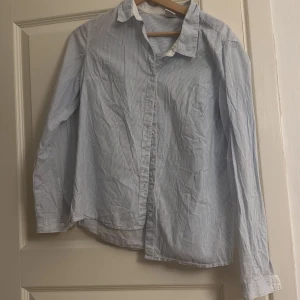 Blårandig skjorta i bomull - Klassisk skjorta med smala blå och vita ränder. I storlek L men skulle säga att den är i storlek S. Perfekt för dig som gillar en clean och stilren look.