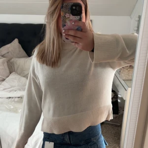 Beige stickad tröja med vida ärmar - Säljer en beige stickad tröja med breda ribbade muddar och lätt croppad passform. Tröjan har lång ärm och en enkel, stilren design som passar perfekt till jeans eller kjol. Supermjuk och skön att ha på sig under kyligare dagar.