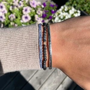 Set med tre armband i blått och silver - Säljer ett snyggt set med tre armband: ett blått flätat band, ett med små svarta och beige pärlor samt ett smalt silverfärgat armband med graverade detaljer. Perfekt att mixa och matcha för en cool och avslappnad stil.