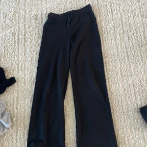 Svarta mjukisbyxor med snörning - Svarta mjukisbyxor med rak passform och snörning i midjan. Perfekta för chill dagar eller när du vill vara extra bekväm. Byxorna har en enkel och stilren look som funkar till det mesta.