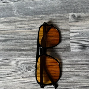 Svarta solglasögon med orange tonade glas - Snygga solglasögon med svart båge och stora, fyrkantiga glas som har en cool orange toning. Perfekta för att sticka ut och ge en modern vibe till din outfit. Helt nya