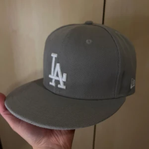 Grå LA Dodgers keps New Era - Snygg grå LA Dodgers keps från New Era med broderad LA-logga framtill och 1988 World Series-märke på sidan. Kepsen har rak skärm och MLB-logga baktill. Tillverkad i bomull, perfekt för dig som gillar sportig streetstyle.